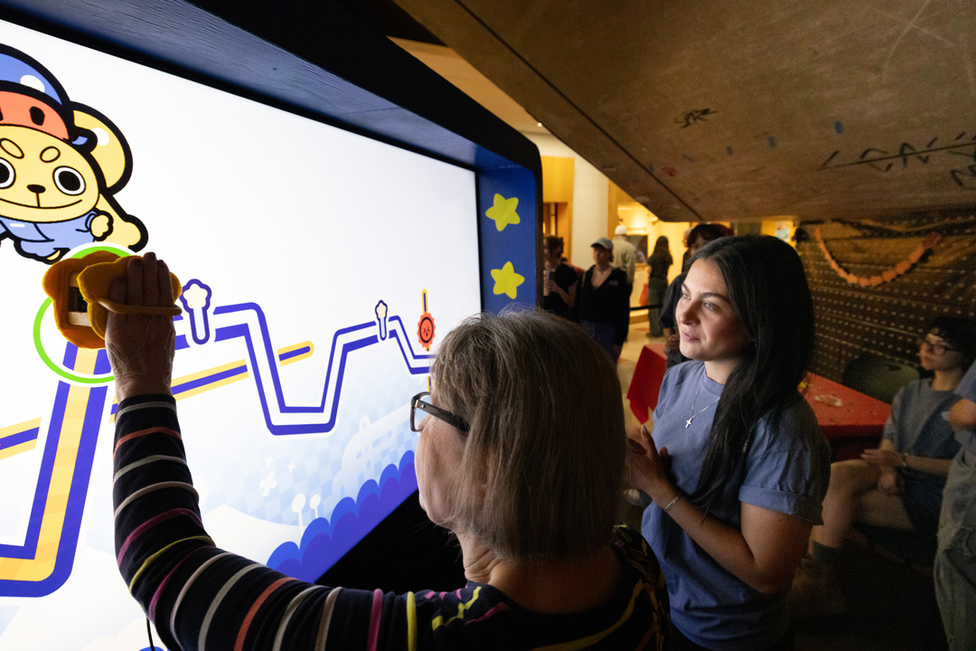 Two participants interact with a large screen showing a game.
